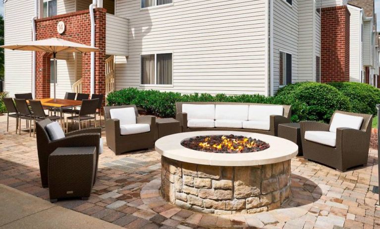 Sonesta ES Suites Annapolis’ patio features a fire pit surrounded by armchairs and a sofa, with a shaded table and chairs nearby.