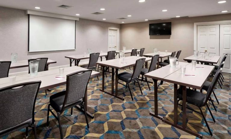 Hotel meeting room, furnished with a wall-mounted TV, and tables arranged in a classroom format facing a projector screen.