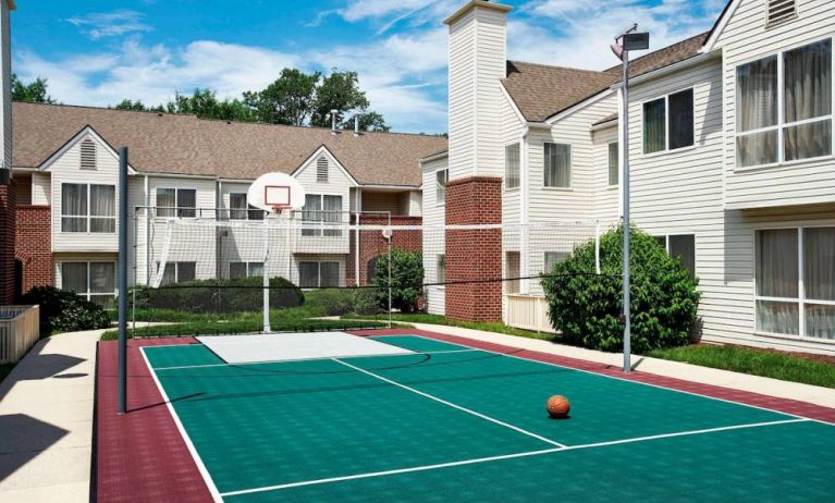 The hotel’s basketball court has a fence by the hoop, and is surrounded by hotel buildings and pleasant greenery.