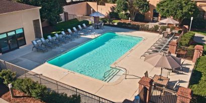 The outdoor pool at Sonesta Select Raleigh Durham Airport Morrisville has sun loungers by the side, as well as shaded tables and chairs.