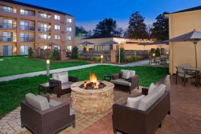 Sonesta Select Raleigh Durham Airport Morrisville’s fire pit has armchair and sofa seating, plus coffee tables, next to it, with shaded tables and chairs nearby.