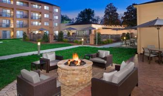 Sonesta Select Raleigh Durham Airport Morrisville’s fire pit has armchair and sofa seating, plus coffee tables, next to it, with shaded tables and chairs nearby.