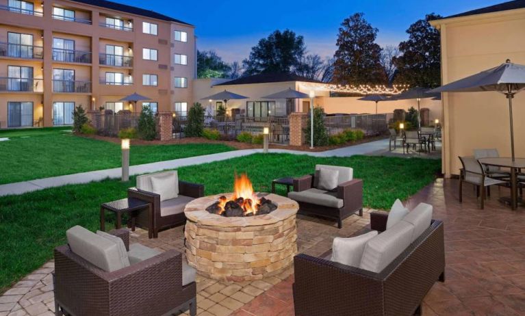 Sonesta Select Raleigh Durham Airport Morrisville’s fire pit has armchair and sofa seating, plus coffee tables, next to it, with shaded tables and chairs nearby.