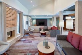 Sonesta Select Raleigh Durham Airport Morrisville’s lobby lounge is furnished with comfy chairs, coffee tables, and sofas, plus a fireplace and TV.