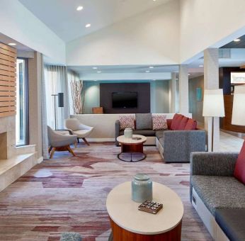 Sonesta Select Raleigh Durham Airport Morrisville’s lobby lounge is furnished with comfy chairs, coffee tables, and sofas, plus a fireplace and TV.