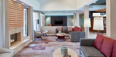 Sonesta Select Raleigh Durham Airport Morrisville’s lobby lounge is furnished with comfy chairs, coffee tables, and sofas, plus a fireplace and TV.