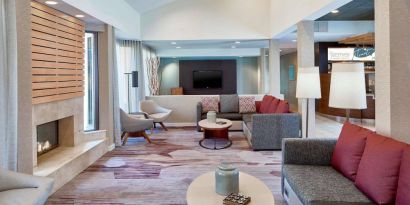 Sonesta Select Raleigh Durham Airport Morrisville’s lobby lounge is furnished with comfy chairs, coffee tables, and sofas, plus a fireplace and TV.