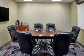 Hotel meeting room, with a wooden table surrounded by six leather chairs, a wall-mounted TV, and a whiteboard.