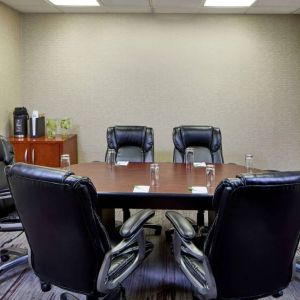 Hotel meeting room, with a wooden table surrounded by six leather chairs, a wall-mounted TV, and a whiteboard.