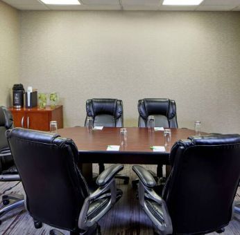 Hotel meeting room, with a wooden table surrounded by six leather chairs, a wall-mounted TV, and a whiteboard.