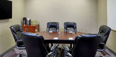 Hotel meeting room, with a wooden table surrounded by six leather chairs, a wall-mounted TV, and a whiteboard.