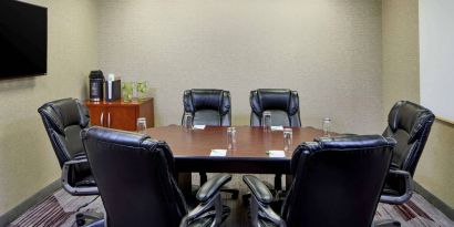 Hotel meeting room, with a wooden table surrounded by six leather chairs, a wall-mounted TV, and a whiteboard.