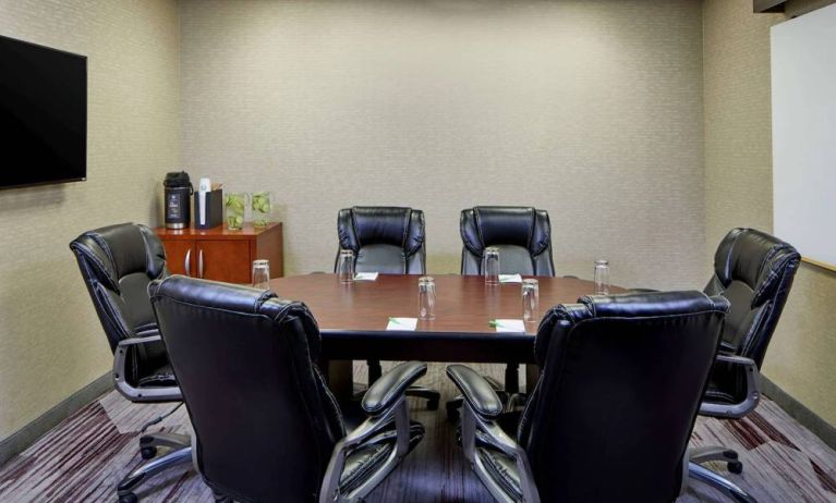 Hotel meeting room, with a wooden table surrounded by six leather chairs, a wall-mounted TV, and a whiteboard.