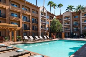 Sonesta Select Phoenix Camelback’s outdoor pool has sun loungers by the side, a shaded area, and tall palm trees.