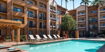 Sonesta Select Phoenix Camelback’s outdoor pool has sun loungers by the side, a shaded area, and tall palm trees.