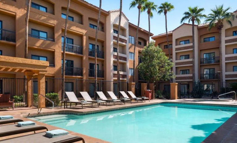 Sonesta Select Phoenix Camelback’s outdoor pool has sun loungers by the side, a shaded area, and tall palm trees.