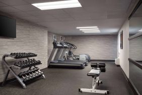 The fitness center at Sonesta Select Phoenix Camelback is equipped with free weights, a range of exercise machines, and a wall-mounted television.