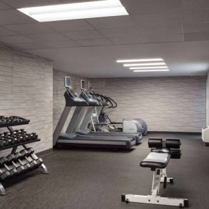 The fitness center at Sonesta Select Phoenix Camelback is equipped with free weights, a range of exercise machines, and a wall-mounted television.