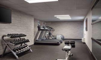 The fitness center at Sonesta Select Phoenix Camelback is equipped with free weights, a range of exercise machines, and a wall-mounted television.