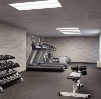 The fitness center at Sonesta Select Phoenix Camelback is equipped with free weights, a range of exercise machines, and a wall-mounted television.