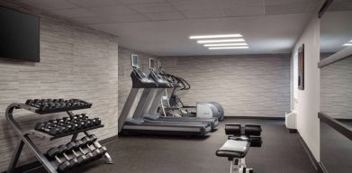 The fitness center at Sonesta Select Phoenix Camelback is equipped with free weights, a range of exercise machines, and a wall-mounted television.