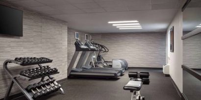 The fitness center at Sonesta Select Phoenix Camelback is equipped with free weights, a range of exercise machines, and a wall-mounted television.