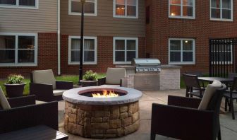 The fire pit at Sonesta ES Suites Raleigh Cary has armchairs around it, a barbecue, and potted plants.