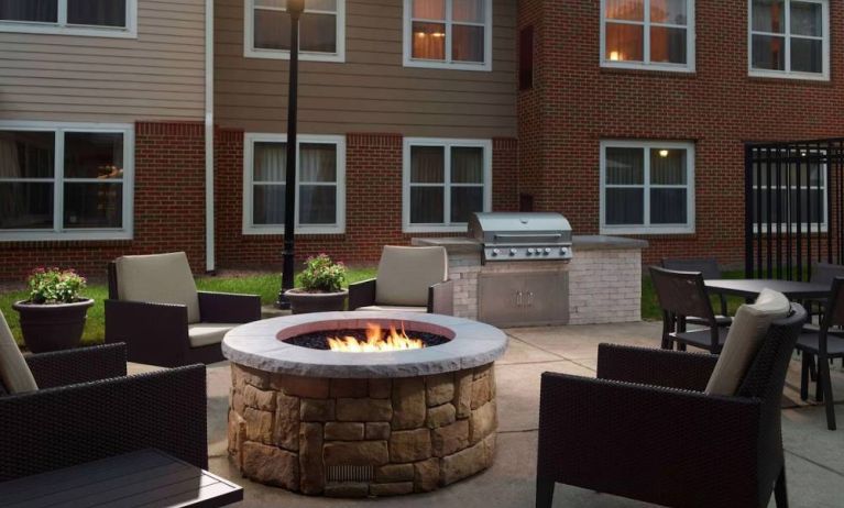 The fire pit at Sonesta ES Suites Raleigh Cary has armchairs around it, a barbecue, and potted plants.