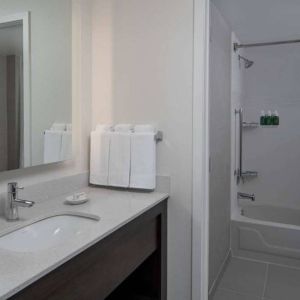 Guest bathroom in Sonesta ES Suites Fairfax Fair Lakes, with shower-equipped bath, mirror, and sink.