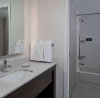 Guest bathroom in Sonesta ES Suites Fairfax Fair Lakes, with shower-equipped bath, mirror, and sink.