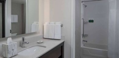 Guest bathroom in Sonesta ES Suites Fairfax Fair Lakes, with shower-equipped bath, mirror, and sink.