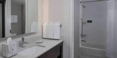 Guest bathroom in Sonesta ES Suites Fairfax Fair Lakes, with shower-equipped bath, mirror, and sink.