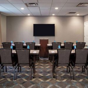 Hotel meeting room, with tables and twelve seats facing a lectern and wall-mounted TV.