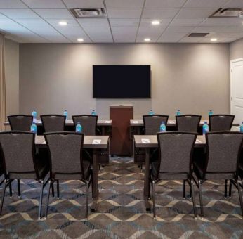 Hotel meeting room, with tables and twelve seats facing a lectern and wall-mounted TV.