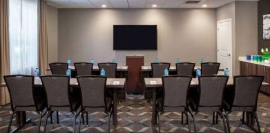 Hotel meeting room, with tables and twelve seats facing a lectern and wall-mounted TV.