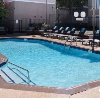 Sonesta ES Suites Dallas Medical Market Center’s outdoor pool has sun loungers as well as armchairs and coffee tables by its side.