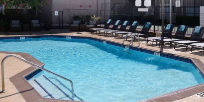 Sonesta ES Suites Dallas Medical Market Center’s outdoor pool has sun loungers as well as armchairs and coffee tables by its side.