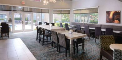 Sonesta ES Suites Dallas Medical Market Center’s lobby is furnished with a mix of table sizes and both regular and tall chairs, with plenty of natural light flowing through large windows.