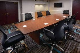 Hotel meeting room, with long wooden table, eight swivel chairs, and a wall-mounted television.