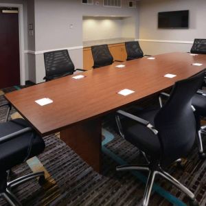 Hotel meeting room, with long wooden table, eight swivel chairs, and a wall-mounted television.