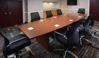 Hotel meeting room, with long wooden table, eight swivel chairs, and a wall-mounted television.