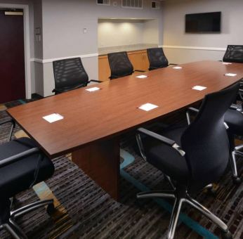 Hotel meeting room, with long wooden table, eight swivel chairs, and a wall-mounted television.