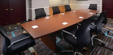 Hotel meeting room, with long wooden table, eight swivel chairs, and a wall-mounted television.