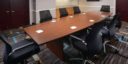 Hotel meeting room, with long wooden table, eight swivel chairs, and a wall-mounted television.