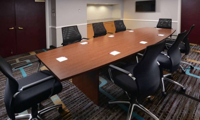 Hotel meeting room, with long wooden table, eight swivel chairs, and a wall-mounted television.