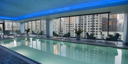 Royal Sonesta Chicago River North’s indoor pool features floor-to-ceiling windows and tables and chairs, and loungers, by the side.