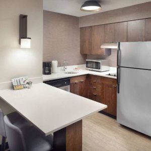 Guest room kitchen in Sonesta ES Suites Raleigh Durham Airport Morrisville, featuring fridge-freezer, hob, microwave, and table.