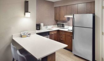 Guest room kitchen in Sonesta ES Suites Raleigh Durham Airport Morrisville, featuring fridge-freezer, hob, microwave, and table.