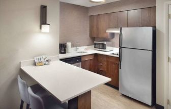 Guest room kitchen in Sonesta ES Suites Raleigh Durham Airport Morrisville, featuring fridge-freezer, hob, microwave, and table.