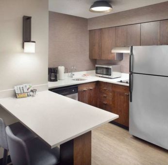 Guest room kitchen in Sonesta ES Suites Raleigh Durham Airport Morrisville, featuring fridge-freezer, hob, microwave, and table.